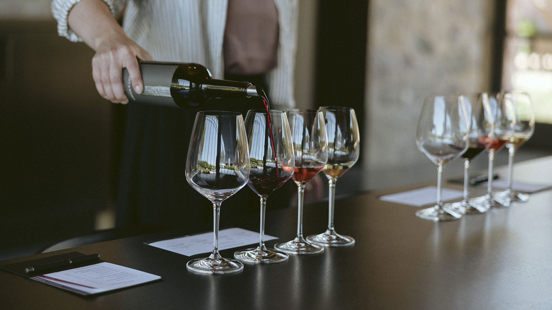 A server pouring red wine into one of several stemmed glasses lined up for a Private Seated Tasting.